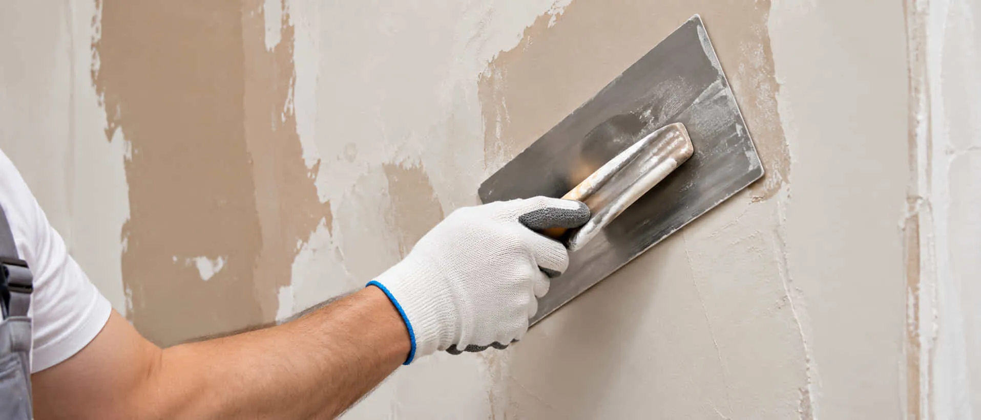 Gloved hand smoothing plaster onto a wall with a steel trowel