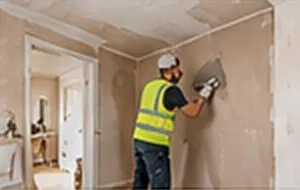 Plasterer in hi-vis skimming a wall in a period room